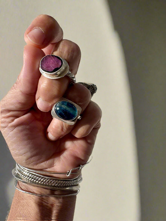 Hand wearing multiple silver rings with gemstones on a light background