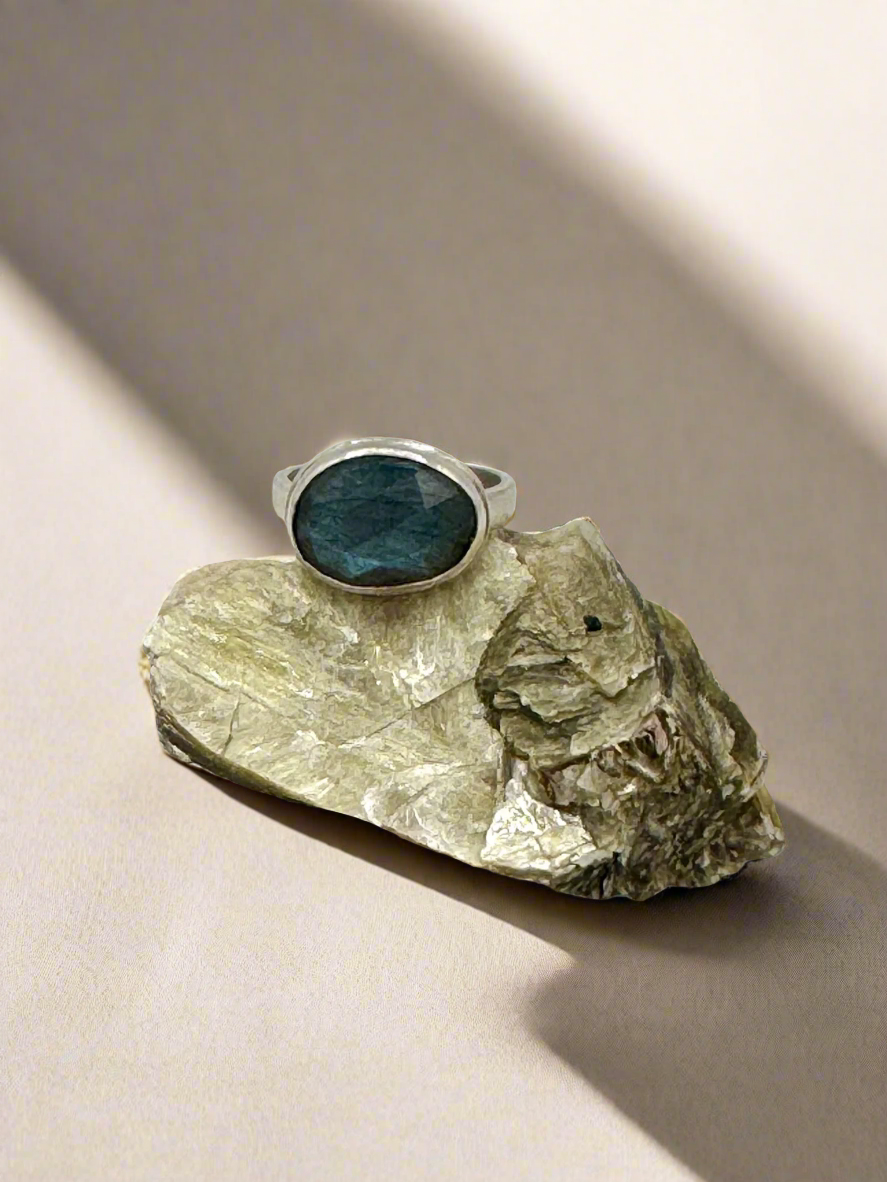 Ring with a labradorite stone on a piece of rock against a gray background