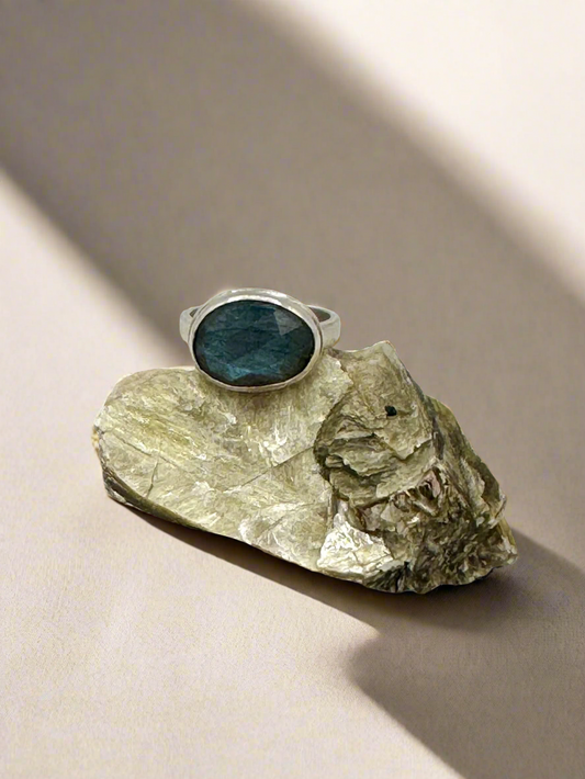 Ring with a labradorite stone on a piece of rock against a gray background